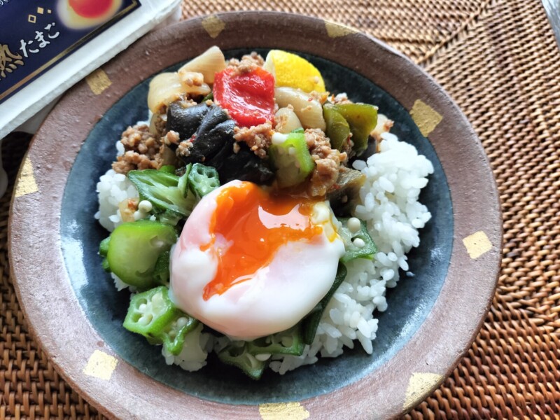 真っ赤な黄身の濃熟たまごを温泉卵にし、赤・緑・黄色の彩り野菜とタイ風スパイスの挽き肉を盛り付けた丼ぶり。金色の器と自然光で高級感を演出したインスタ映え料理。