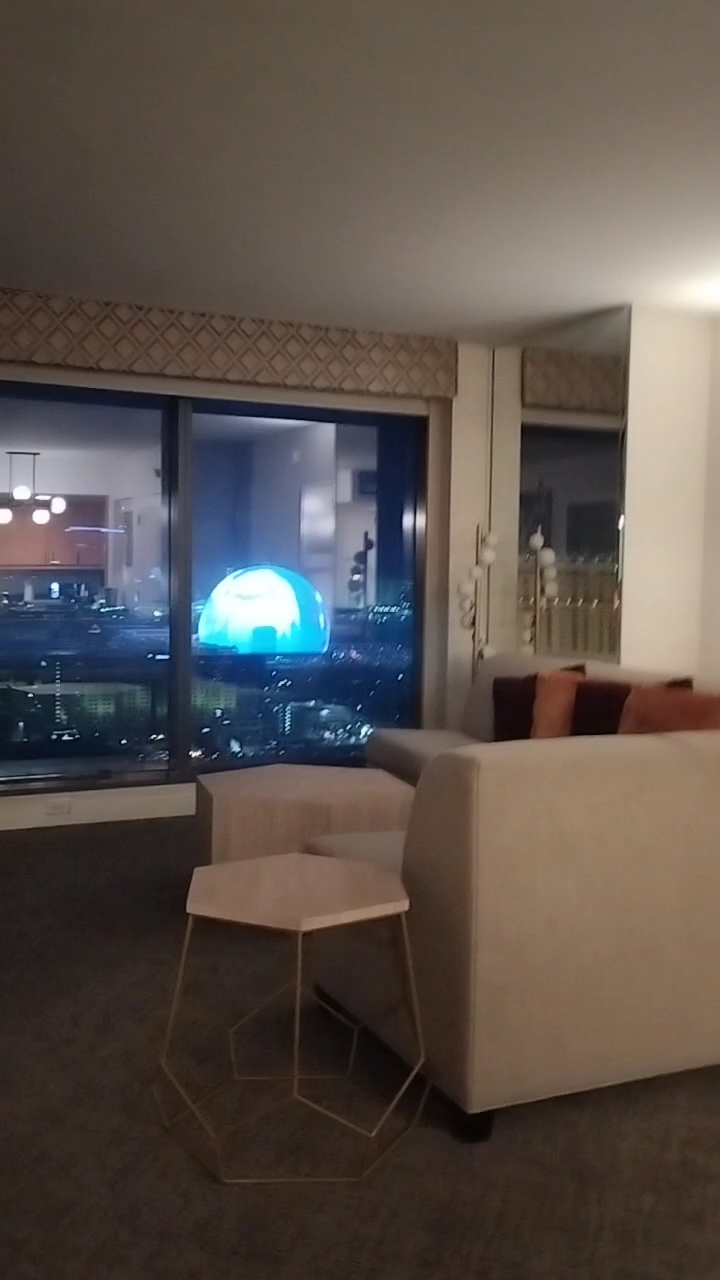 ラスベガスの高層ホテルの部屋から見えるスフィアの夜景。リビングと大きな窓越しに映る最新エンターテインメント施設の眺望。