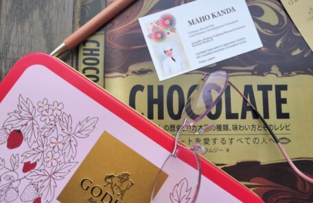 チョコレートの専門書と英語版名刺を使った商品開発研究のイメージ